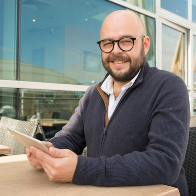 smiling-middle-aged-man-using-tablet-street-cafe_1262-19056.webp